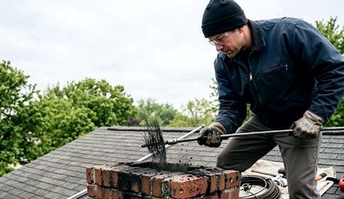 Sweep clearing a chimney under a low grey sky