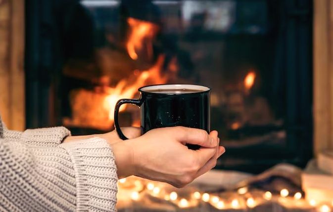 Warm mug cradled before a burning fireplace